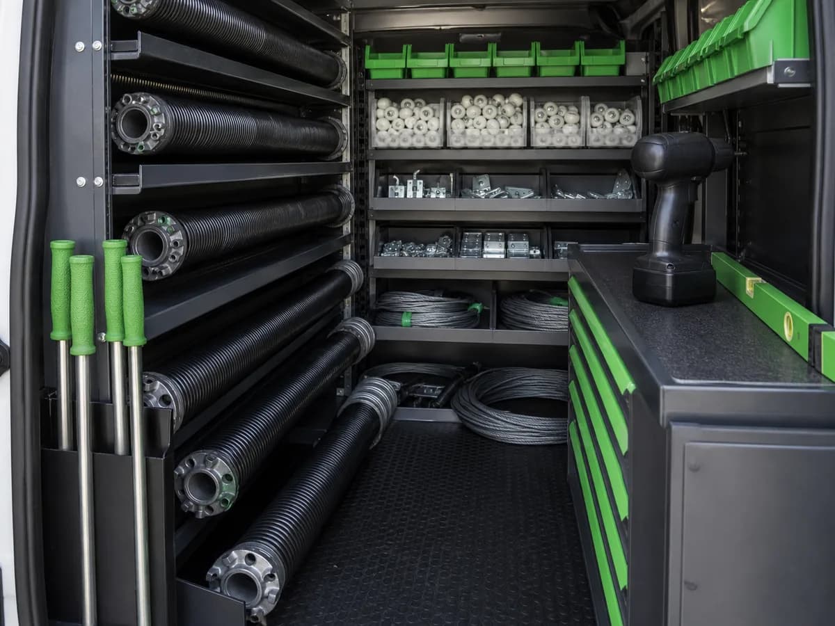 The organised interior of a garage door service vehicle with torsion springs, rollers, cables and winding bars